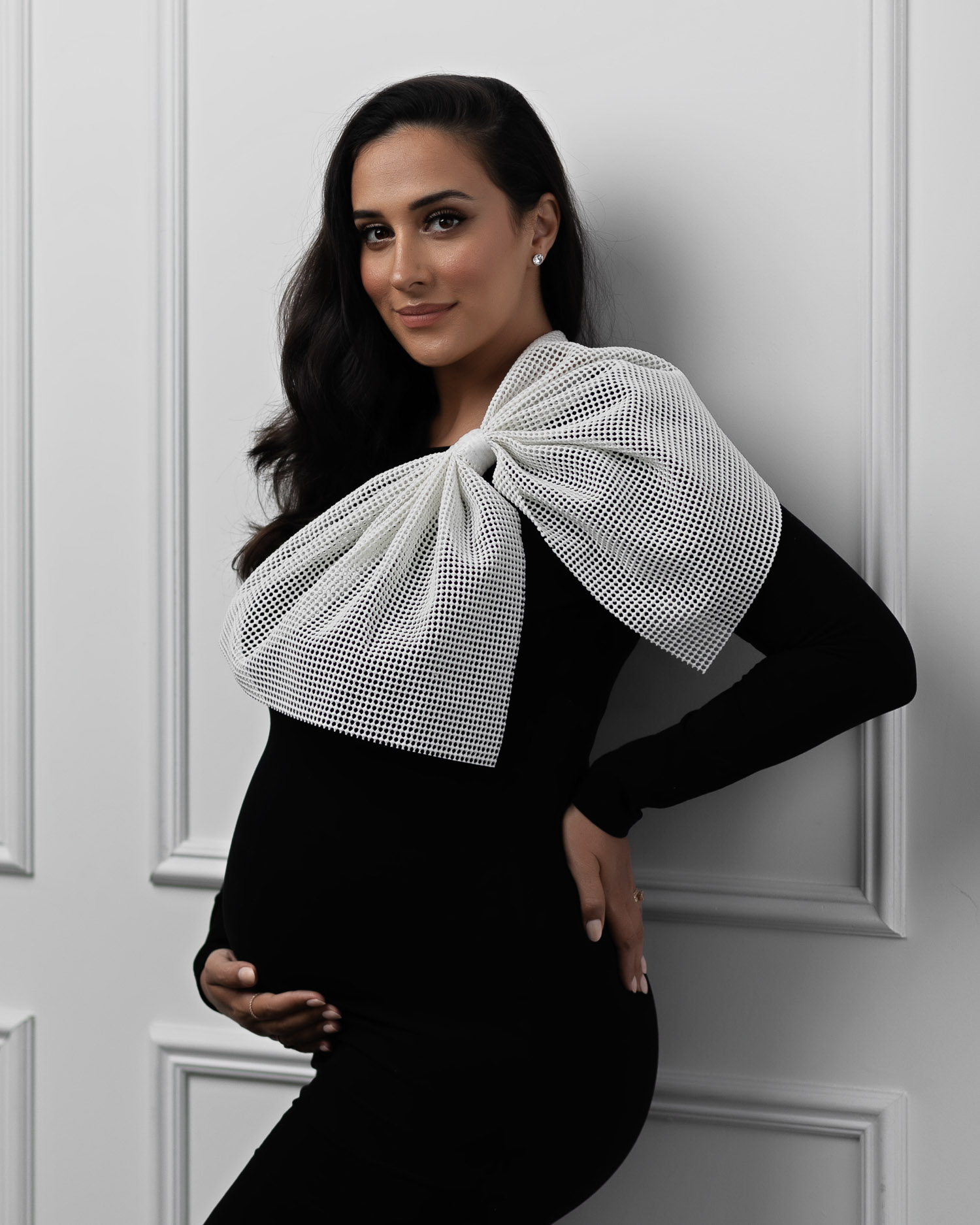Pregnant woman wearing a black dress with a white bow.