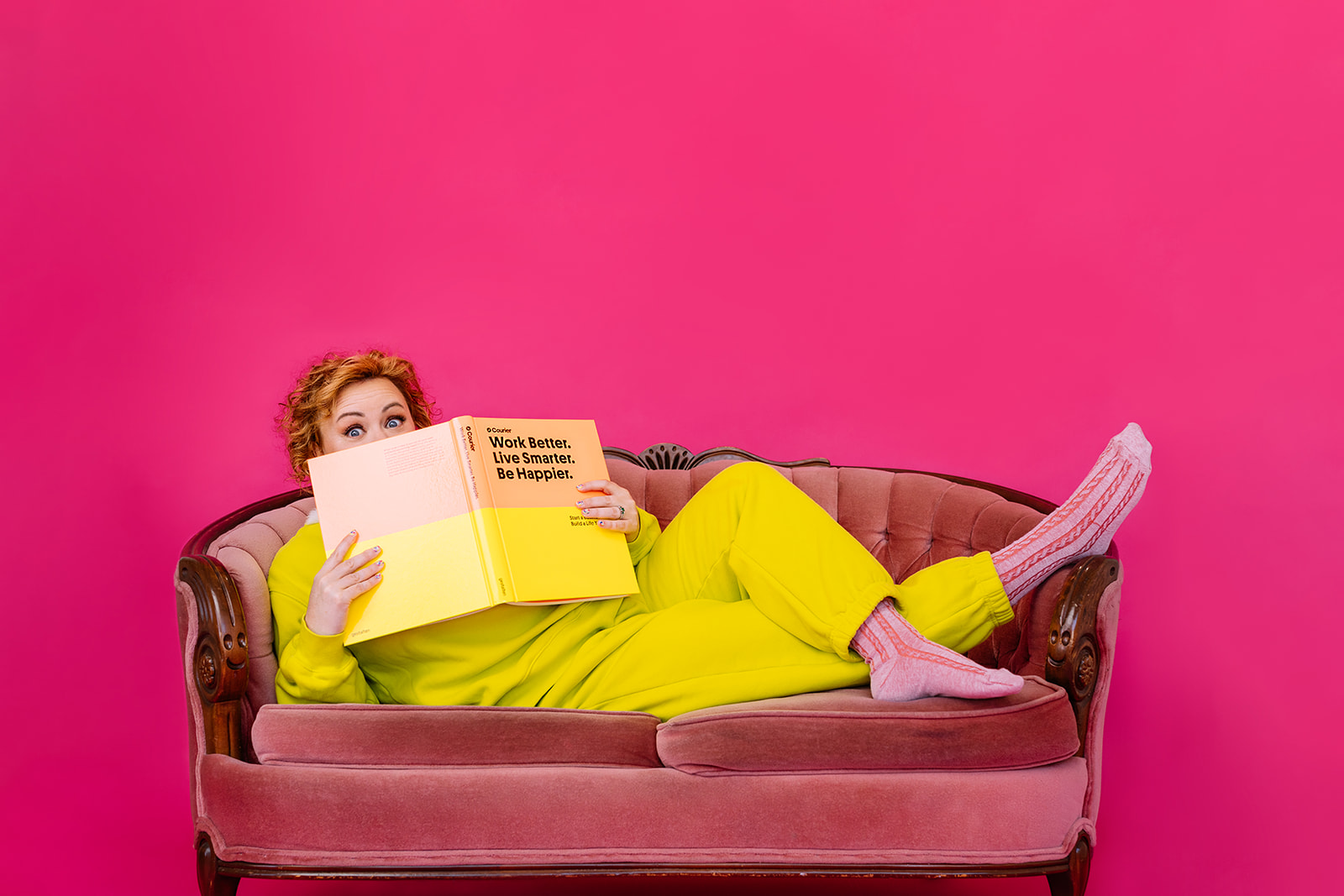 business coach on a sofa reading a book wearing neon yellow outfits in a pink backdrop